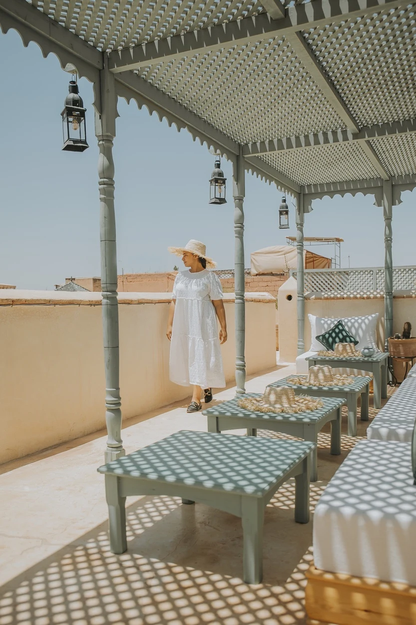 Une femme en robe blanche marche sous la pergola de la terrasse